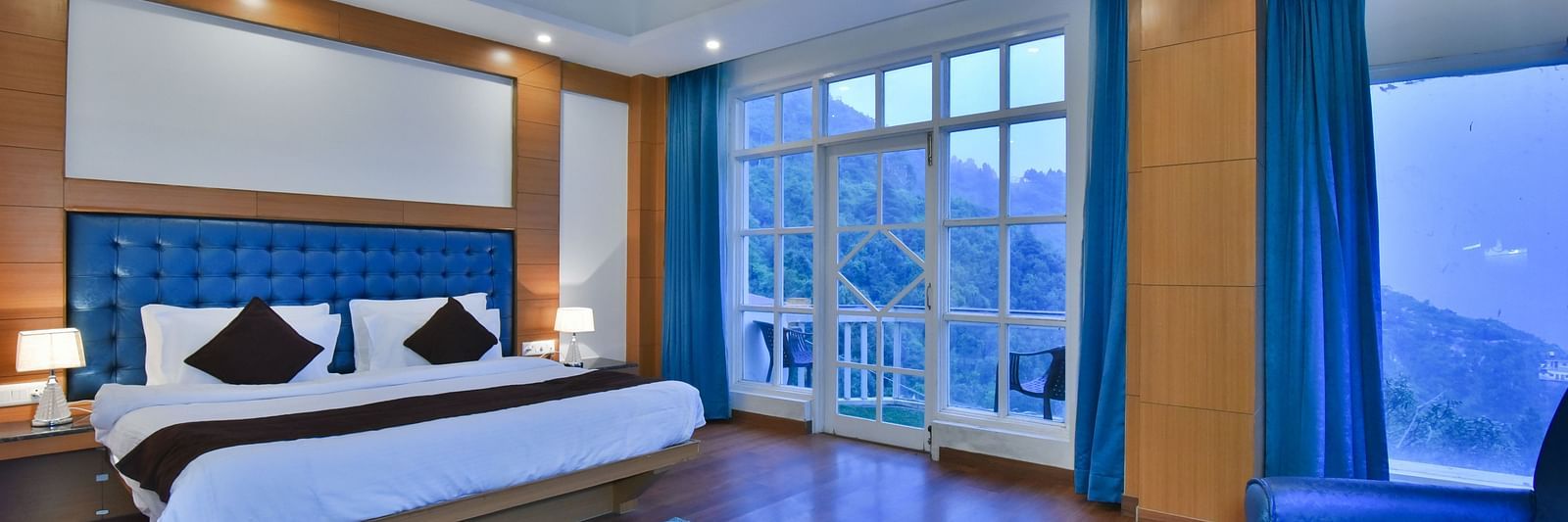 A large bed placed in front of the sofas in Luxury Room with Balcony at DLS Highland Resort and Spa, Mussoorie.